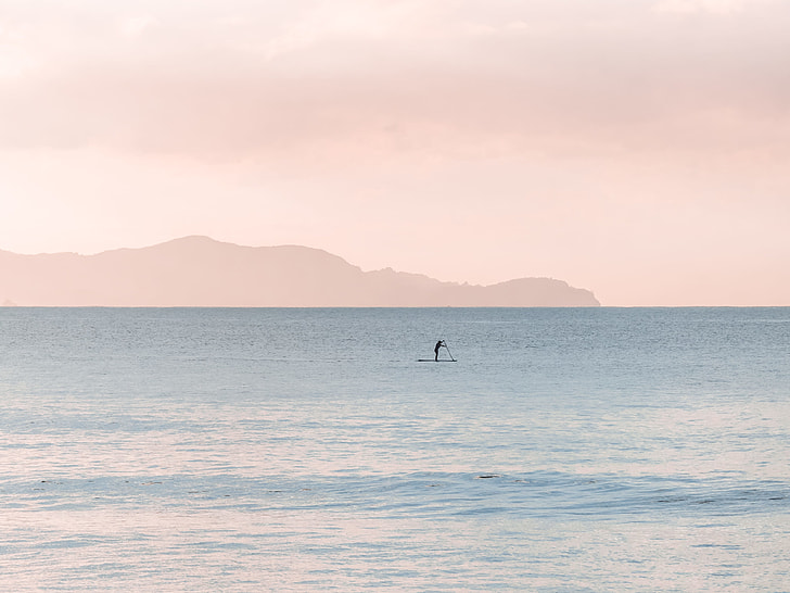 person standing on paddle board and rowing using a paddle on far distance