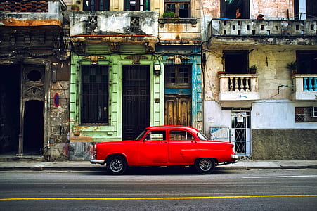 classic red coupe beside gray concrete building during daytime