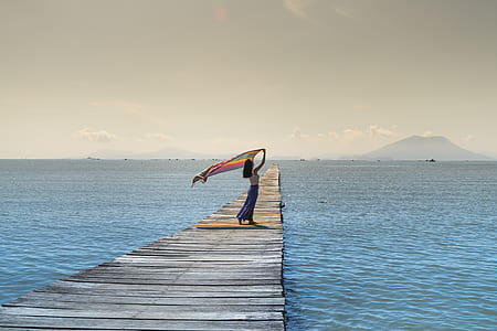 woman holding textile standing on gray wooden sea dock during daytime
