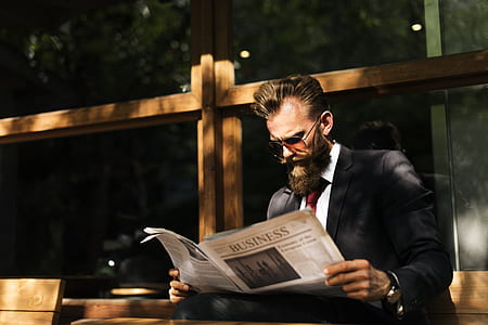 man wearing black and white tuxedo suit reading newspaper during daytime