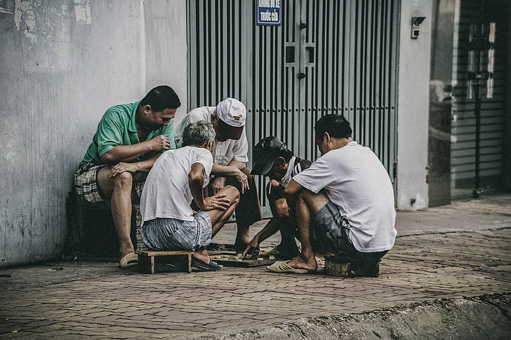 three men watching two men playing board game on street during daytime