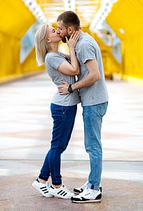 kissing couple in gray shirts with denim jeans and white-and-black shoes during daytime