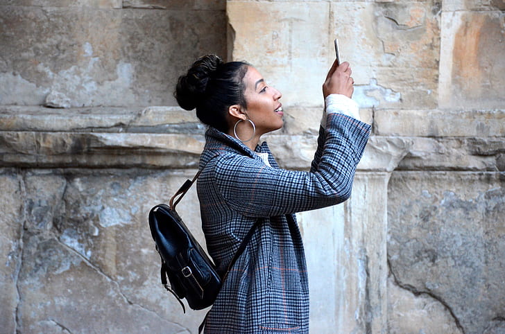 woman holding her phone near brown wall