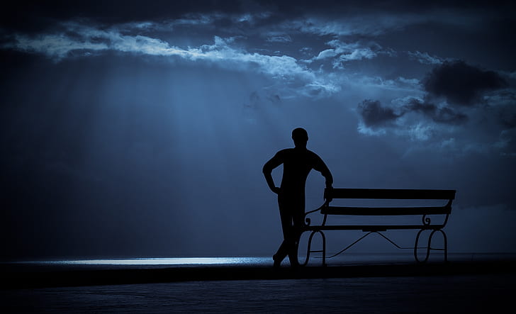 silhouette of man besides bench under cloudy sky