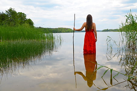 photo of woman wearing red dress holding stick in body of water