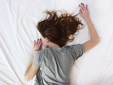 woman wearing gray t-shirt sleeping on white bed comforter
