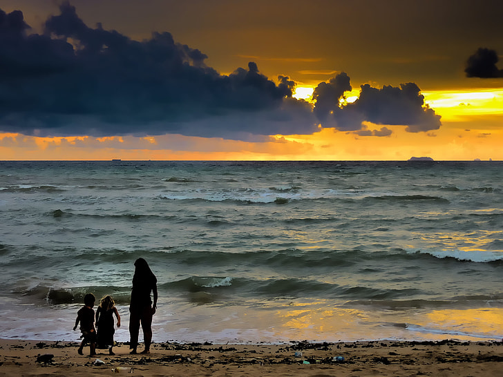 silhouette of woman and two toddlers on seashore