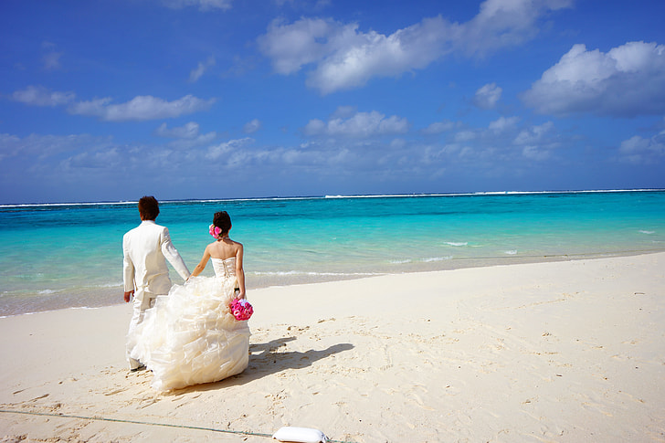 newly wedding couple walks on shoreline during daytime