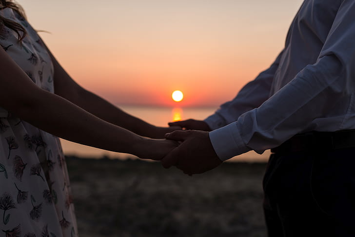 man and woman holding hands during sunset