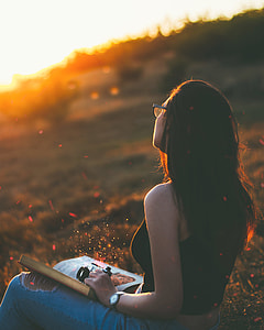 book on woman's lap sitting on grass during golden hour