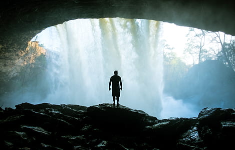 silhouette of man standing in cave fronting water falls