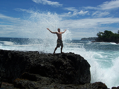 man standing on rock beside body of water