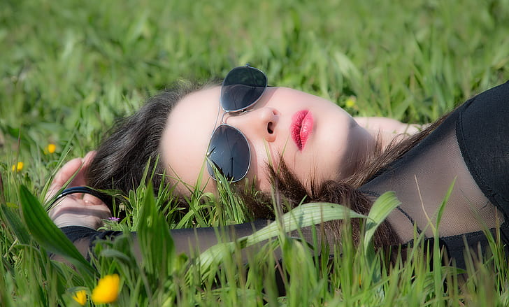 woman wearing black long-sleeved top and black aviator-style sunglasses lying on grass during daytime