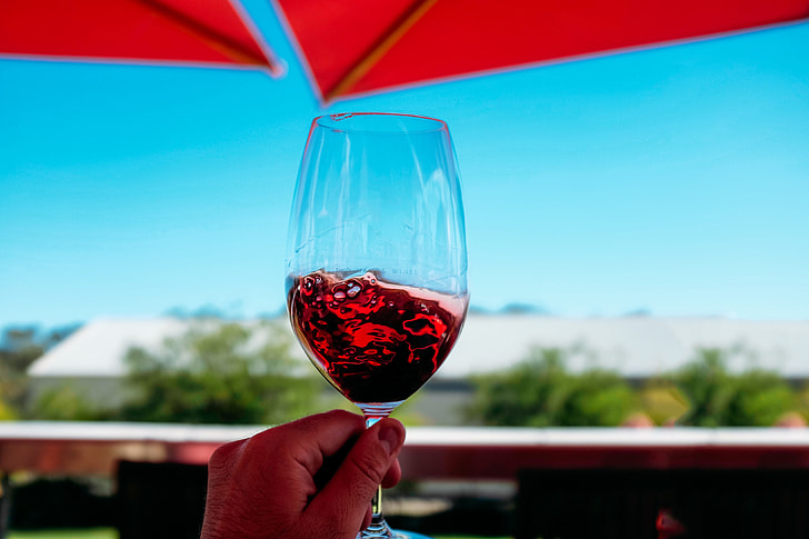 Glass of red wine being held against a blue sky