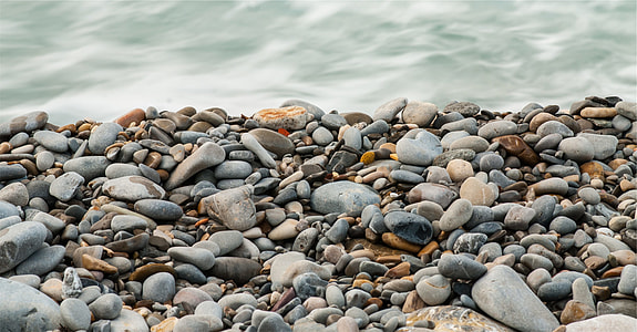 depth of field photography of sea shore pebbles near sea wave