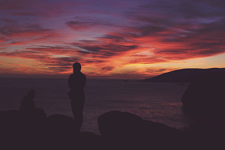 silhouette photo of man standing near rock during golden hour