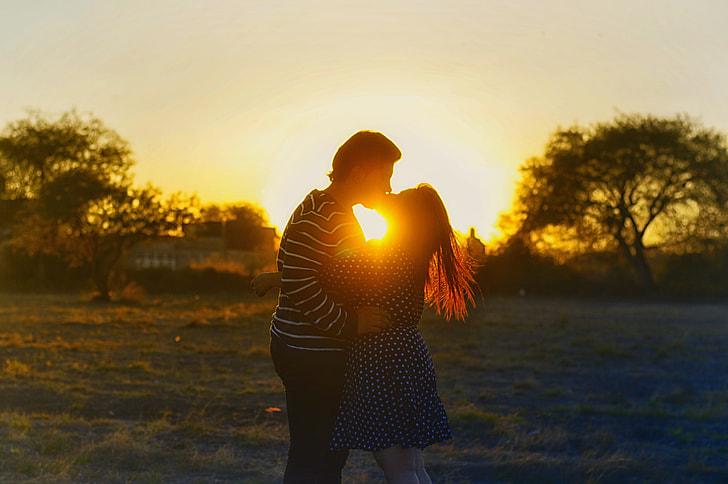 couple kissing on grass field during sunset