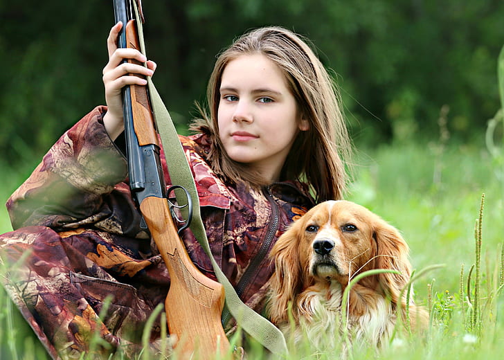 woman with red tree camouflage suit holding brown hunting rifle beside orange and white Welsh springer spaniel on grass field during daytime