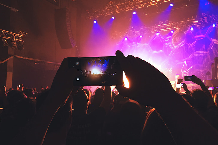 A person photographer in the crowd taking a photo with their mobile phone at a music concert festival