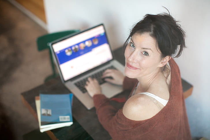 woman wearing brown off-shoulder sweatshirt while using MacBook