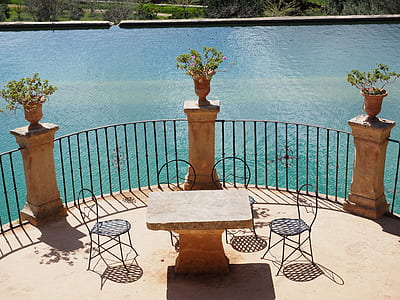 brown concrete table with 4-chairs beside body of water during daytime