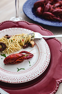 Fancy dinner with seafood pasta, crayfish and red wine by the table decorated with roses