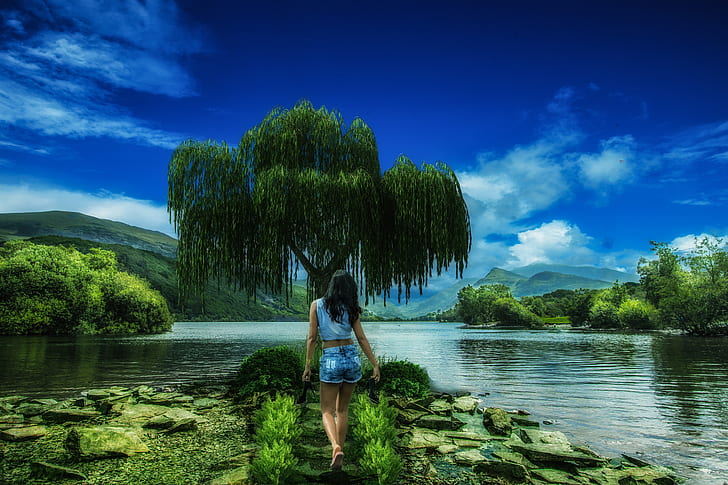 woman wearing blue sleeveless shirt standing near green willow tree