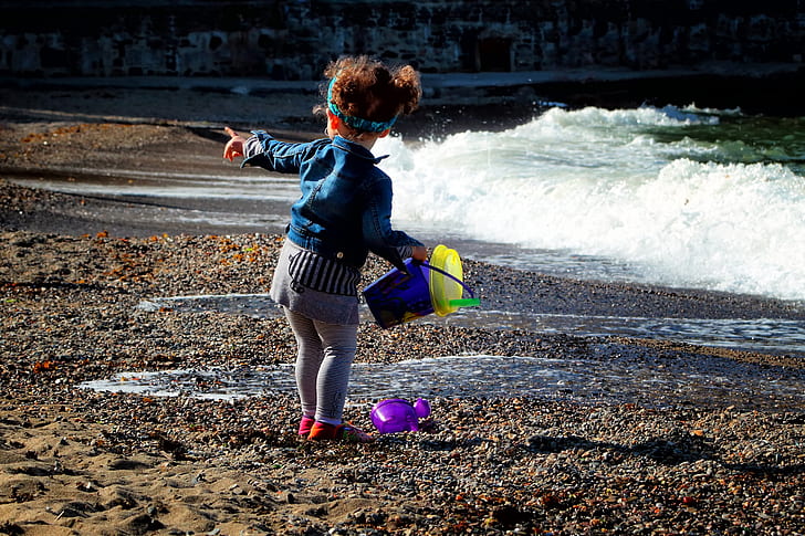 toddler in jacket holding bucket standing on seashore