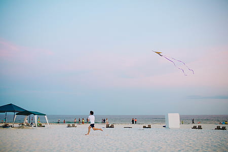 man wearing white shirt running holding kite under cloudy sky