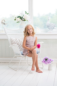girl sitting on armchair holding pink petaled flower