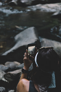 woman holding smartphone while taking photo of waterfalls