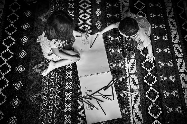 grayscale photography of two children holding color pens