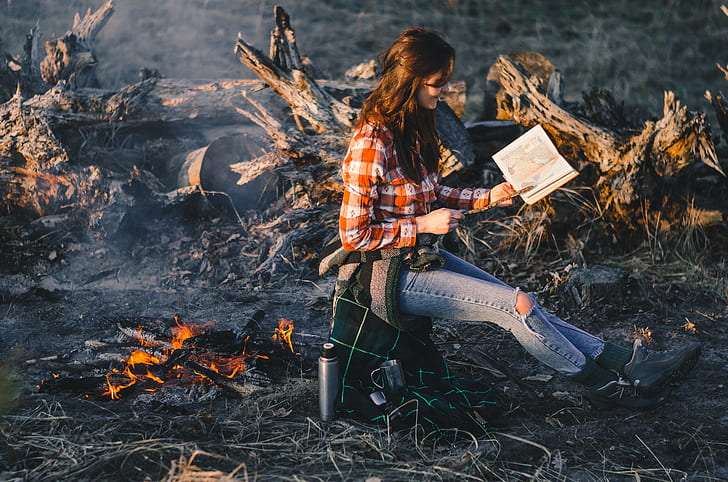 shallow focus photography of woman near bonfire reading book