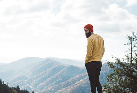 A man with a beard and hat near mountains