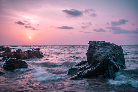 timelapse photo of sea waves crashing on grey stones at sunset