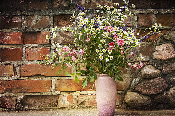 pink rose flowers, white aster flowers, and lavender flowers in pink vase beside brown bricked wall