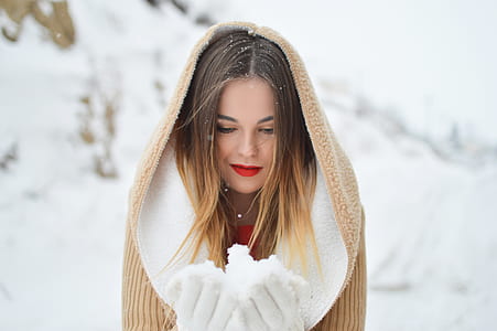 shallow focus photography of woman in brown coat holding snow