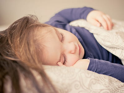 female child wearing blue long-sleeve shirt sleeping in bed