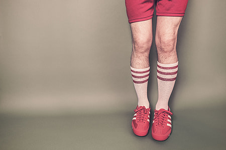 portrait of a person's legs wearing a pair of red adidas sneakers and pair of white-and-red high socks