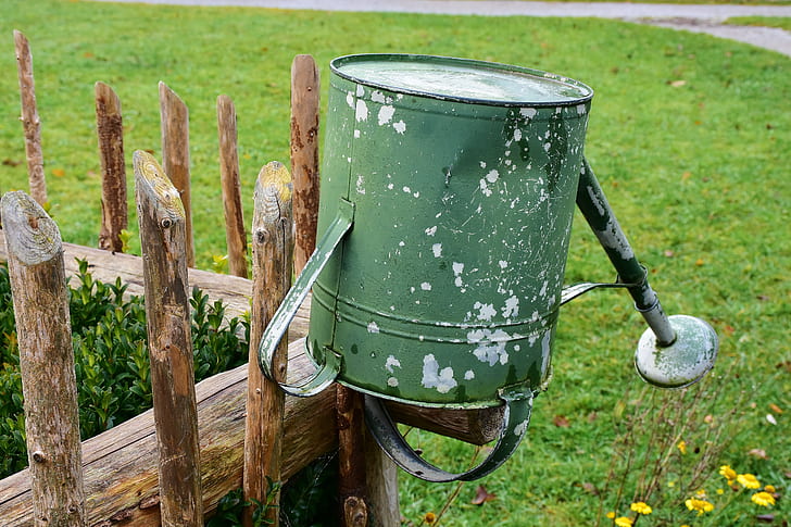 green steel watering can on brown wooden fence