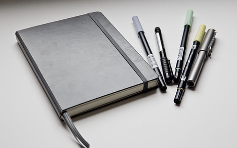 black leather notebook and five pens
