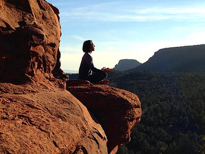 person meditating on brown rock formation