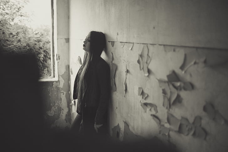 greyscale photo of woman leaning on wall during daytime