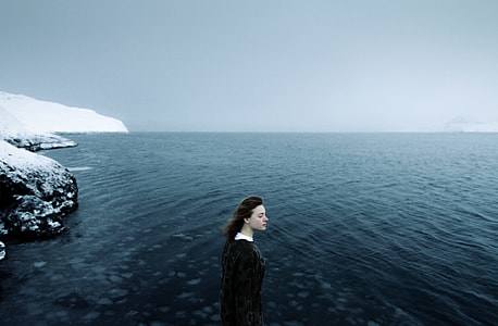 girl in black dress standing on sea shore filled with snow