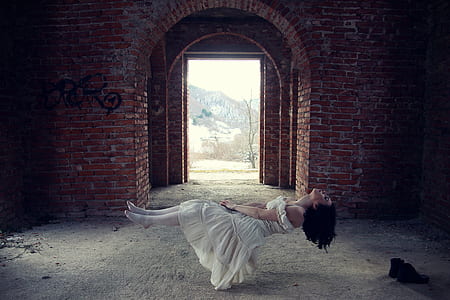 woman in white dress floating inside red brick building at daytime