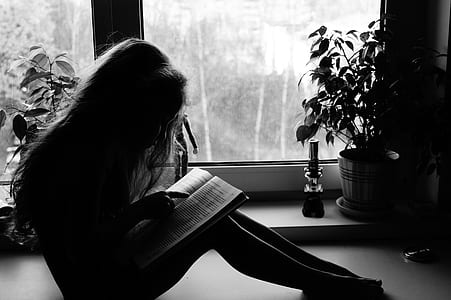 girl reading book in grayscale photography