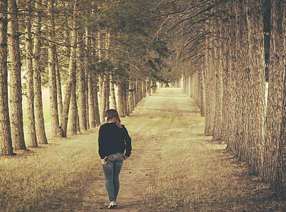 Woman Wearing Black Longsleeve and Gray Jeans Walking on Brown Forest