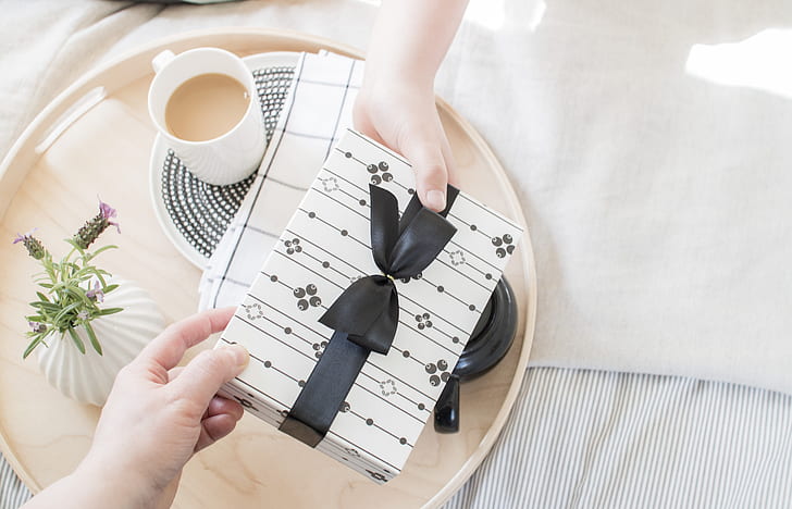 two people's hands holding white and black gift box