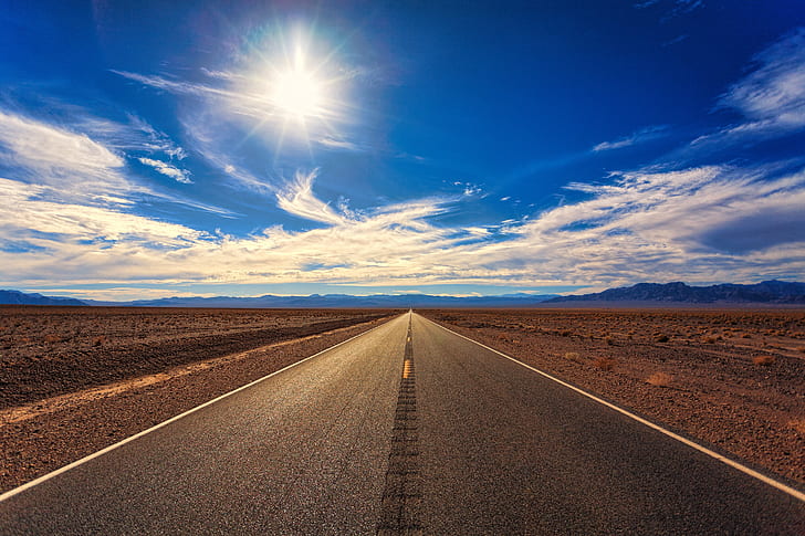 gray asphalt road between desert field during daytime