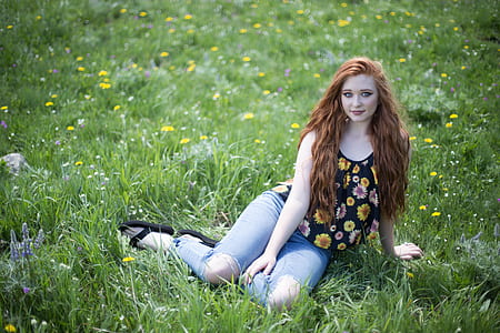 woman wears black and multicolored floral scoop-neck tank top sits on green grass fiel
